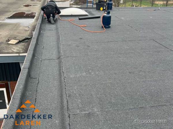 Dakdekker repareert bitumen dakbedekking op groot plat dak in Laren