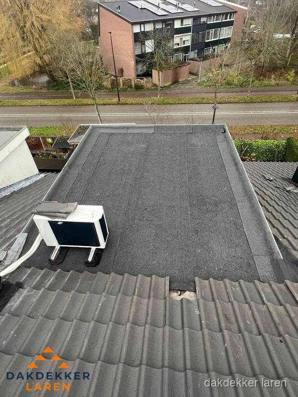 Plat dak inspectie met bitumen bedekking naast schuin pannendak in Laren