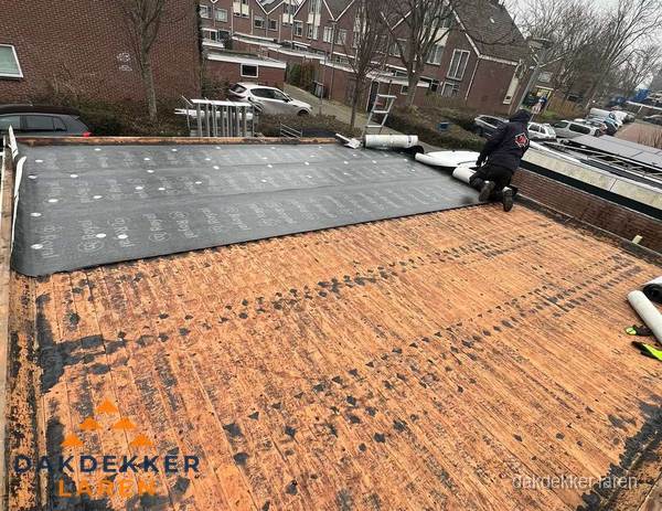 Dakdekker legt onderlaag op plat dak met houten constructie in Laren