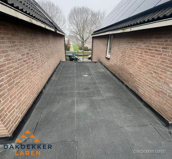 Plat dak met bitumen dakbedekking tussen bakstenen muren in Laren